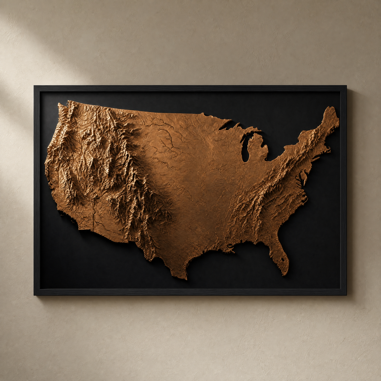 America in Relief bronze topographic map print in a slim matte black frame on a warm greige wall — the whole country in sculptural relief, ready to hang.